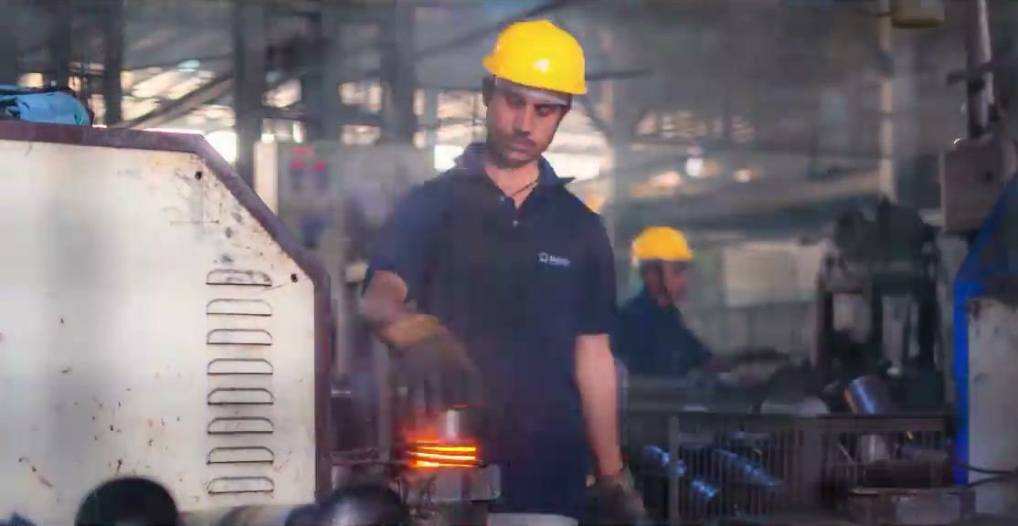 A Rajlaxmi worker in a hard hat over a glowing, induction-heated vessel base
