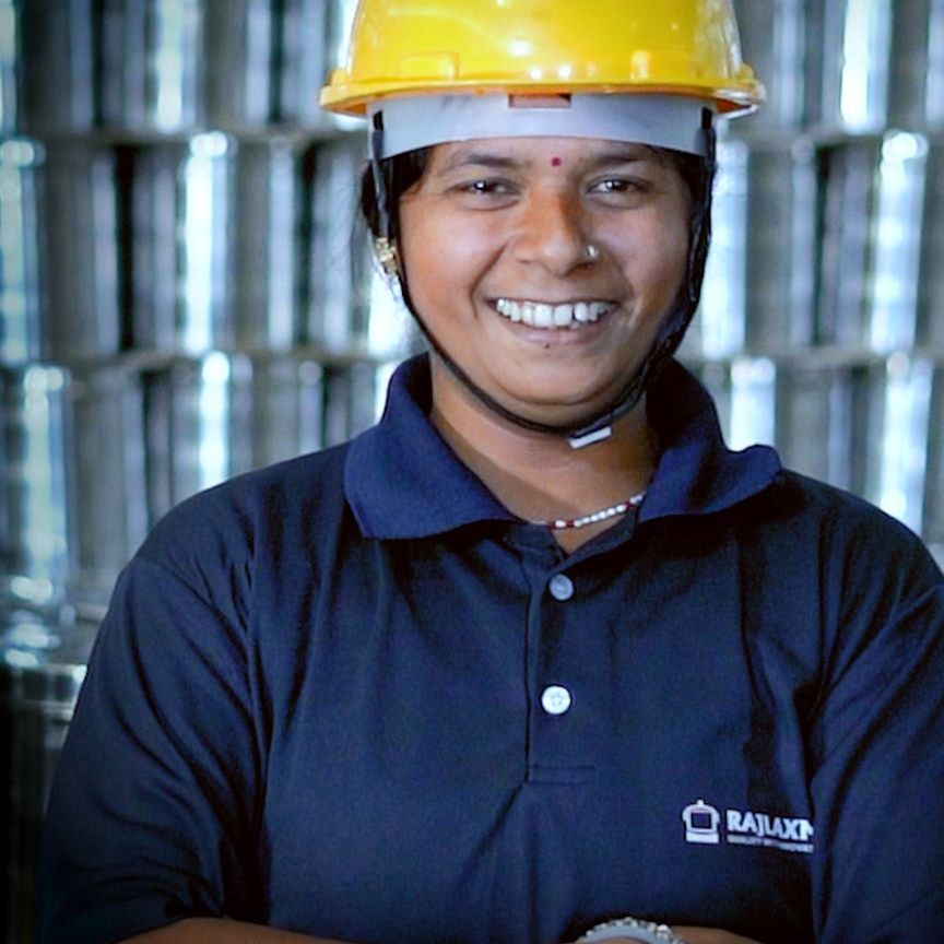 A Rajlaxmi team member in a hard hat in front of stacked steel vessels